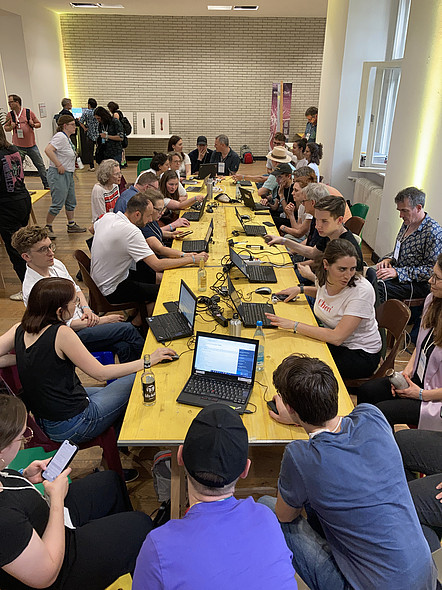 Die Workshop Teilnehmenden sitzen an einem großen Tisch mit Laptops vor sich.